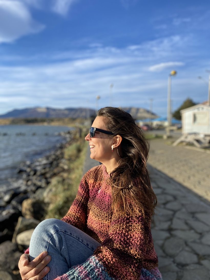 Mari sentada junto al mar, mirando hacia un costado